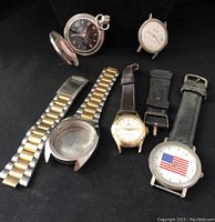 Overall view of watch parts including pocket watch head, wristwatch heads, and bands on black background.
