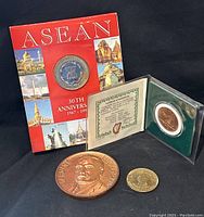 Photo of all four coins together showing the ASEAN coin in packaging, the large copper penny, and the two smaller coins.
