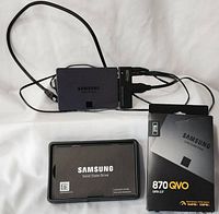 Samsung 870 QVO SSD with USB to SATA adapter and original packaging, manual, and cords displayed on white background.