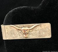 Front view of the gold embossed longhorn steer's head on the silver money clip with floral engraving