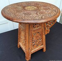 Three-quarter view of the carved wooden table showing detailed floral patterns on top and on the folding legs.
