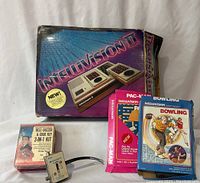 Intellivision II boxed console with Pac-Man and Bowling cartridges, Bell Buzzer & Code Key 3-in-1 Kit, and Archer Game switch.
