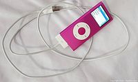 Pink iPod Nano with screen turned on, showing music menu and connected to charger cable.