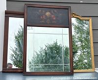 Three vintage wall hung mirrors outside showing full front views, including the Edmonds floral oil painted mirror with etched glass, gold art deco mirror, and wooden framed mirror.