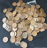 Top-down image showing a large pile of used wheat penny coins on a black background.