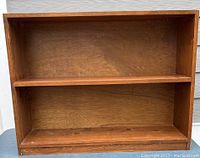 Full front view of wooden bookshelf showing one fixed shelf and wood grain finish.