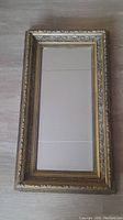Full view of antique rectangular framed mirror with detailed gold floral and ornamental edges laid flat showing overall condition and design.