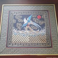 Full front view of framed embroidered rank badge on black fabric background with ornamental border and central bird design