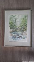 Full view of framed watercolour painting showing landscape with flowing creek and surrounding trees and rocks