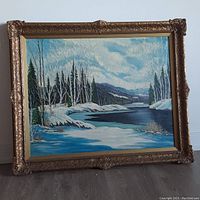 Frontal view of the large framed oil painting showing the winter landscape scene with snow, river, trees, and mountains.