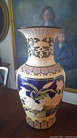 Front view of the tall ceramic floor vase, showing detailed bird and flower motif on dark blue base with a flared cream rim featuring black scrollwork.