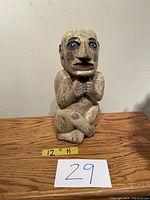 Front view of a 12-inch tall carved and painted wooden man figurine from Guatemala showing the full figure seated cross-legged with hands clasped.