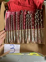 Roll-up fabric holder containing 13 spiral drill bits in ascending size order from left to right.