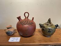 Three assorted Guatemalan pottery vessels on wooden surface against white wall, paper label with number 24