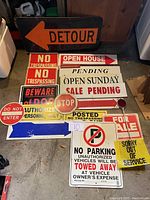Photo showing the collection of assorted vintage traffic and warning signs laid out on a floor including detour, sale pending, open Sunday, stop, no parking, and others.