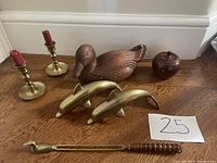 Photo showing all items on wooden floor, including wood carved duck, brass dolphins, brass candle holders with red candles, wood apple container, duck-shaped candle with wooden handle, and candle snuffer.