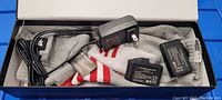 Photo showing gray, white, and red striped heated socks, two black rechargeable batteries, and one black AC power charger inside an open box.