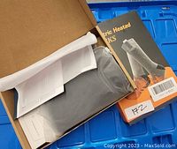 Box containing grey rechargeable electric heated socks with instruction manual included.