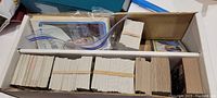 Full view inside a cardboard box containing stacks of sports trading cards, some in ziplock bags and some banded in bundles.