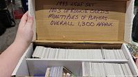 Image showing a cardboard box filled with numerous hockey cards, labeled inside lid with quantity and type (1993 Leaf set, hundreds of rookie cards, multiples of players, approx. 1300 cards).