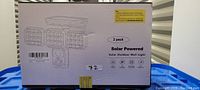 Photo of box showing 2 pack of solar powered outdoor wall lights with motion sensor, retail packaging with basic product features.