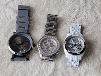 Three watches laid out on a beige textured surface showing brands and distinct designs