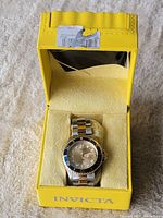 Invicta wristwatch displayed inside original yellow branded box on cushion.