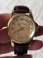 Front view of the Lucien Piccard wristwatch showing gold-tone case, textured dial with Roman numerals and date window, brown leather strap.