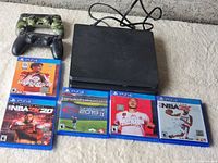 PS4 console with power cord, two controllers, and five PS4 game cases laid out on a soft surface.