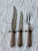 Front view of the three-piece set showing two knives and one fork with silver handles placed on a white textured fabric.