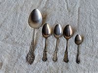 Top view showing all five sterling silver spoons of varying sizes, laid out in order from largest to smallest on a light textured fabric background.