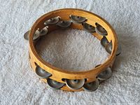 Photo showing the whole wooden tambourine with metal jingles attached around the circular frame resting on a white fabric.