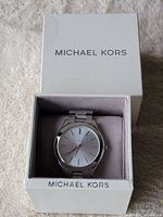 Front angled view of Michael Kors watch inside the original box showing the silver watch face and metal band.