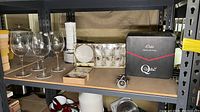Shelf with four Luigi Bormioli wine glasses, boxed wine opener, boxed coffee and tea cup set, and boxed cheese utensils set