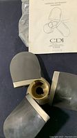 Three-blade propeller with visible hub and edges, shown on a black surface with installation manual.