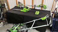 Overview of mower, blower, trimmer, charger and batteries displayed on table.