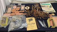 Overview of leather crafting collection showing leather pieces, rivets in plastic bags, leather laces tangled, two booklets, and stamping tools.