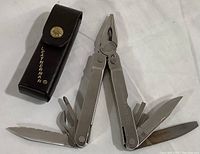 Full view of the Leatherman Super Tool opened showing multiple tool blades and the black leather carrying case beside it
