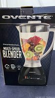Photo of the front of the box showing Ovente branding and image of the blender full of fruit in the pitcher showing design and color.