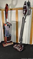 Shark Rocket True Pet upright vacuum and Shark Navigator vacuum placed side by side on black surface with beige curtains backdrop.