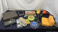 Photo showing assortment of tools and hardware including Black and Decker drill, chargers, gloves, bolts, foam blocks, and light on blue surface