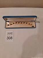 View of the gold-tone bracelet inside original vintage blue box with cream lining, showing the row of amethyst rhinestones in a satin ribbon design