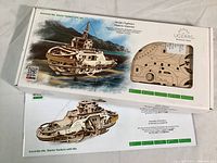 Box front displaying the Ugears Mechanical Tugboat Model with image of completed model and wood sheets visible through window.