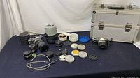 Overview of vintage Olympus camera, lenses, attachments, cases, and Dot Line aluminum train case on a dark cloth surface.