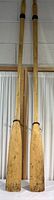Full length view showing two long wooden oars with natural finish, hung vertically.