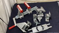 Image showing the Work Shops Vunder Vise parts laid out with the main clamp and several smaller metallic components with red jaw covers.