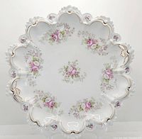 Top down image of porcelain bowl showing hand painted small rose floral clusters evenly spaced inside. Scalloped edge with gold trim and cutouts visible.