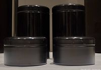 Front view showing 4 black metal canisters with lids, two tall on left and two short on right, arranged in a line.
