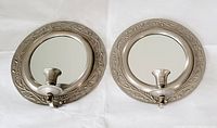 Pair of round hammered tin wall mounted candle holders with inset mirrors and decorative embossed patterns, laid flat on white background