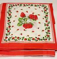 Folded tablecloth showing the central strawberry design and red border with strawberry leaves and small berries.